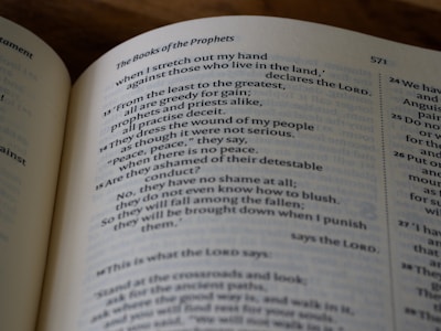 A close-up view of an open book, displaying text from the Books of the Prophets. The text is printed in two columns with verse numbers on the side. The lighting casts a soft shadow, adding depth to the page.