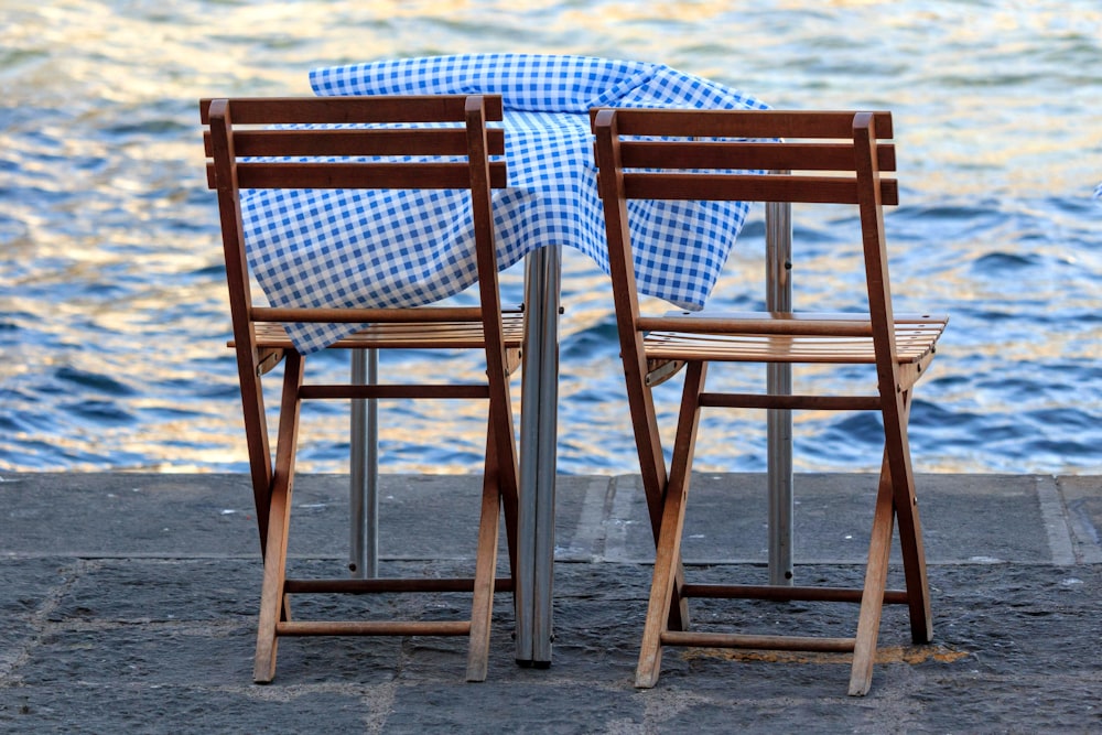 two wooden chairs sitting next to each other near a body of water