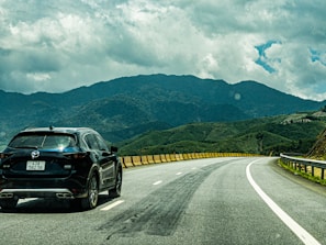 Photo of a black SUV driving on a scenic road surrounded by trees.
