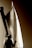 A person wearing a hat is silhouetted against a large sail. The light and shadow create a dramatic contrast on the sailcloth, highlighting its texture and structure. The angle suggests the person is involved in handling or observing the sail, contributing to a nautical theme.