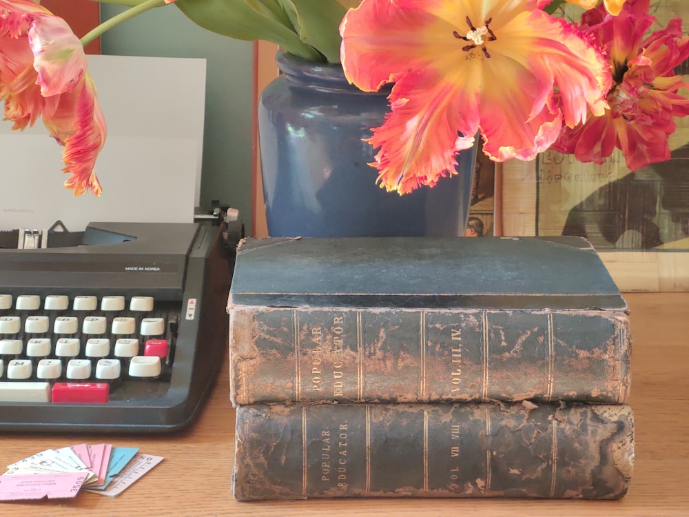a desk with a book, a typewriter and a vase of flowers