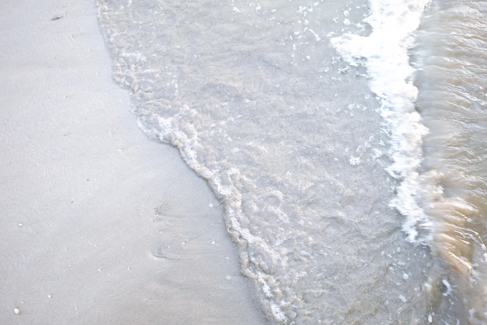 Serene beach scene with light beige sand and crashing white waves against blue sky