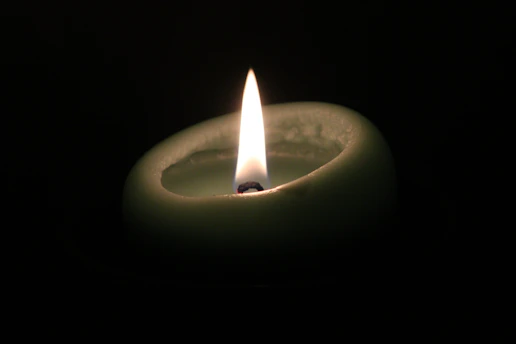 A softly glowing candle flame flickering against a desert night sky with sage green and desert gold hues.