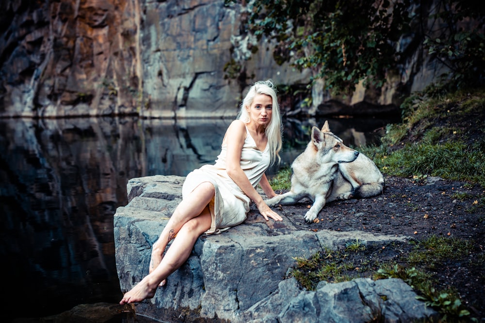 a woman sitting on top of a rock next to a dog