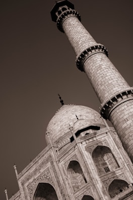 A sepia-toned image highlighting the intricate details of the Taj Mahal. The focus is on one of its minarets and the ornate arches and carvings of the main dome. The architectural grandeur and symmetry of the structure are emphasized.