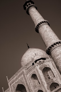 A sepia-toned image highlighting the intricate details of the Taj Mahal. The focus is on one of its minarets and the ornate arches and carvings of the main dome. The architectural grandeur and symmetry of the structure are emphasized.
