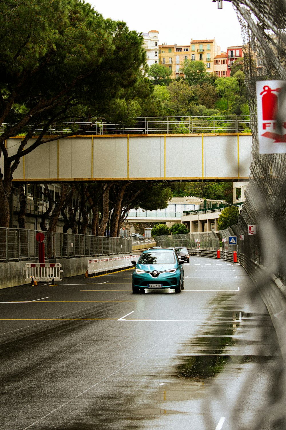 a blue car driving down a street next to a bridge