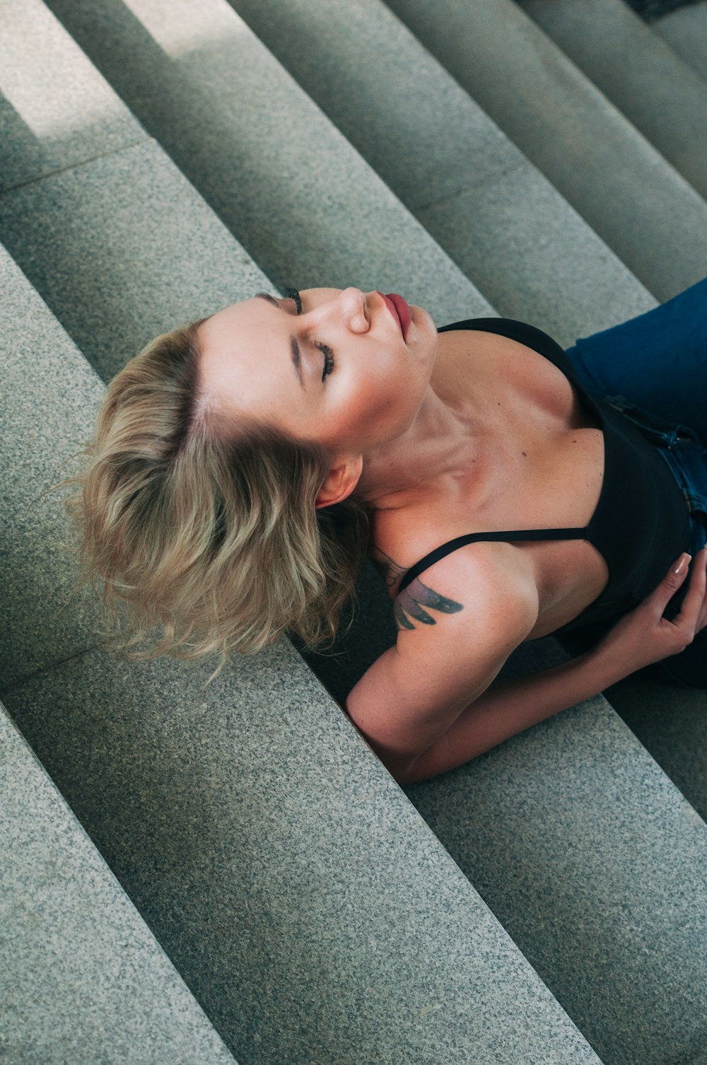 a woman in a black top is laying down on some stairs