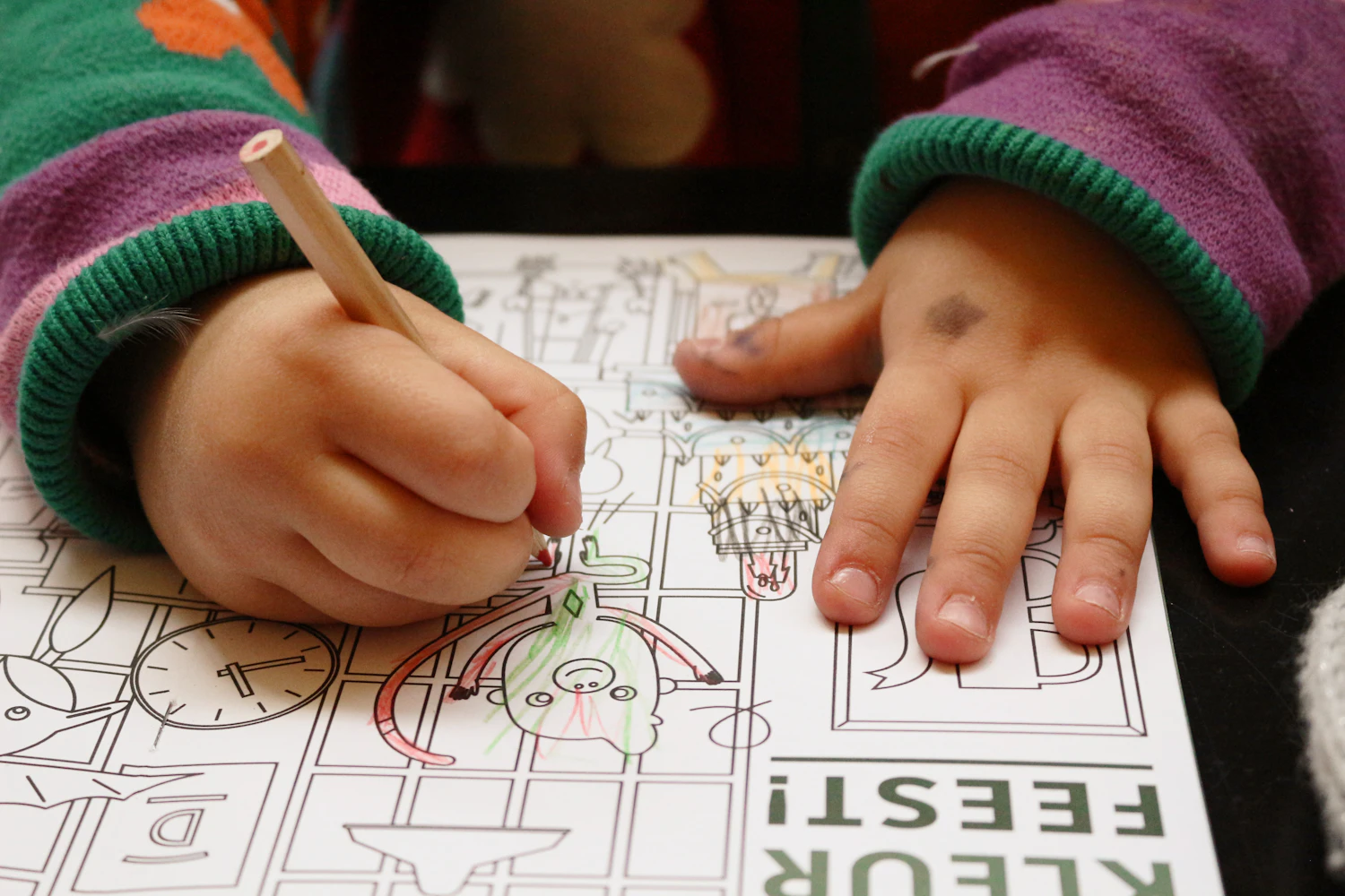 A young child drawing on paper at a table, holding a pencil