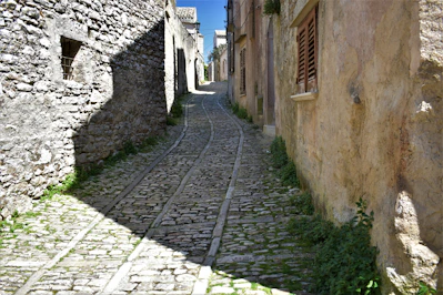 a narrow cobblestone street with a stone building in the background