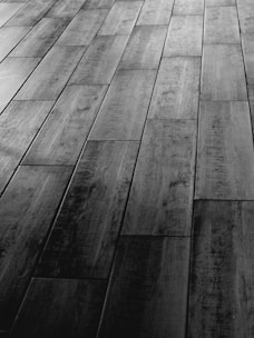 A textured wooden floor with rectangular planks arranged in a staggered pattern. The surface features natural wood grain and shading, creating a sense of depth and dimension.
