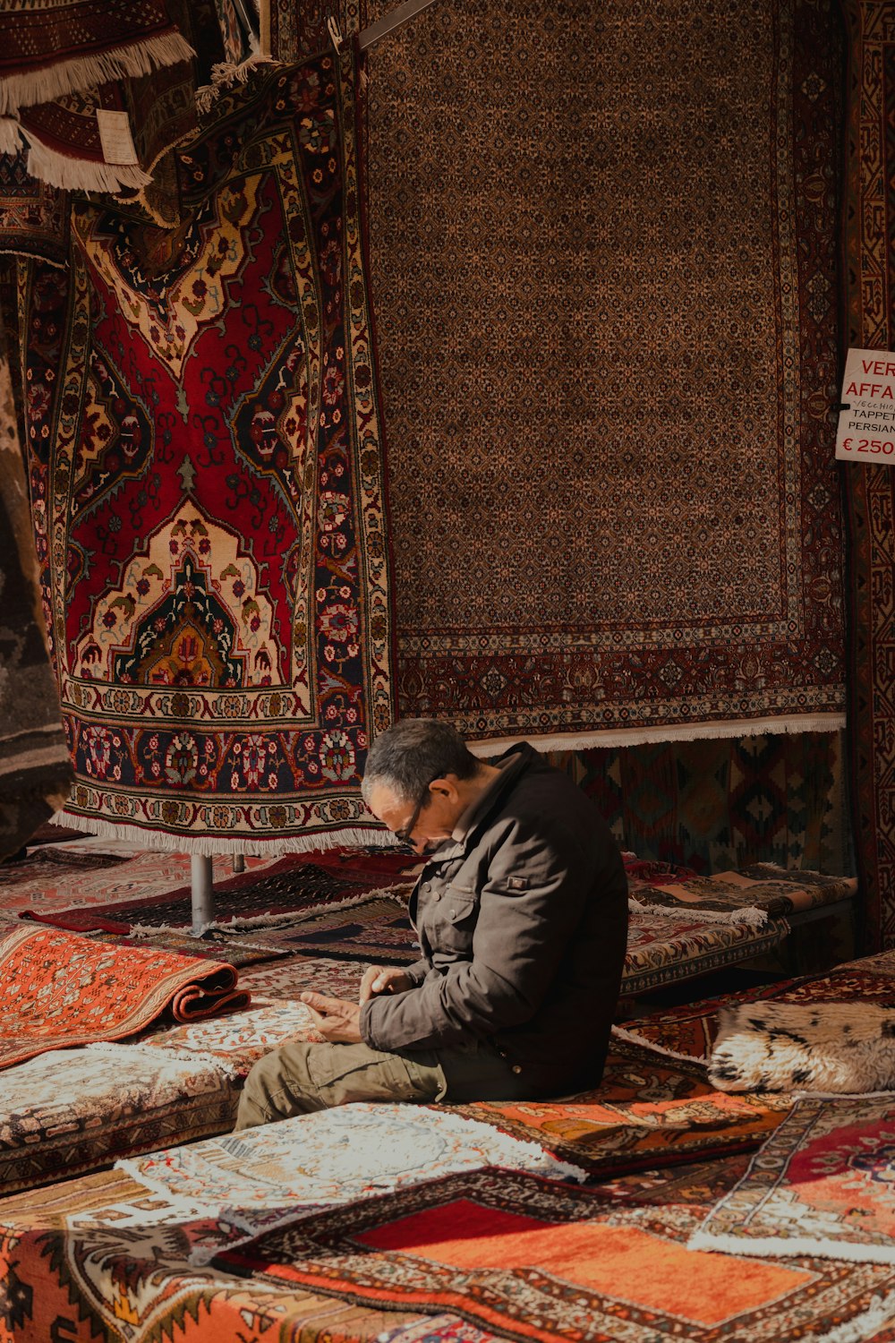 a man sitting on the ground next to a pile of rugs
