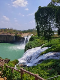 A vibrant turquoise waterfall surrounded by lush green rainforest under a bright blue sky.