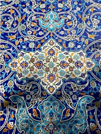 Intricate and colorful ceramic tiles featuring elaborate floral and geometric patterns. The design includes vibrant blue, orange, green, and white colors with detailed, interwoven motifs and decorative blossoms.