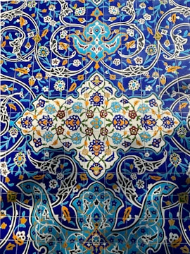 Intricate and colorful ceramic tiles featuring elaborate floral and geometric patterns. The design includes vibrant blue, orange, green, and white colors with detailed, interwoven motifs and decorative blossoms.