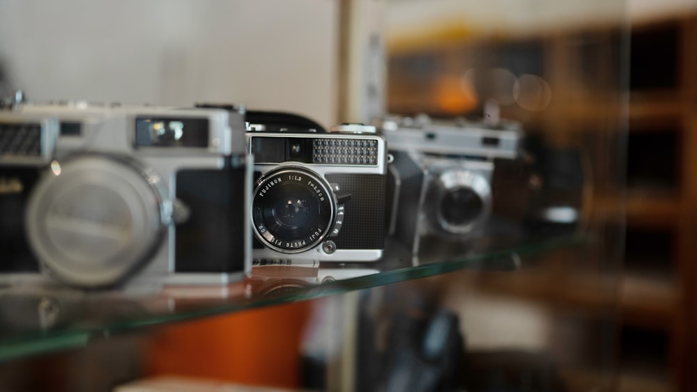 a group of cameras sitting on top of a glass shelf