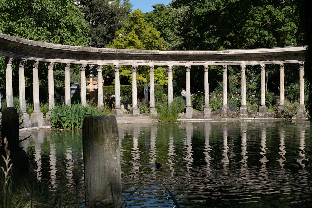 a pond with columns and a bench in the middle of it