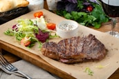 A juicy steak served with fresh salad and rustic bread on a wooden board.