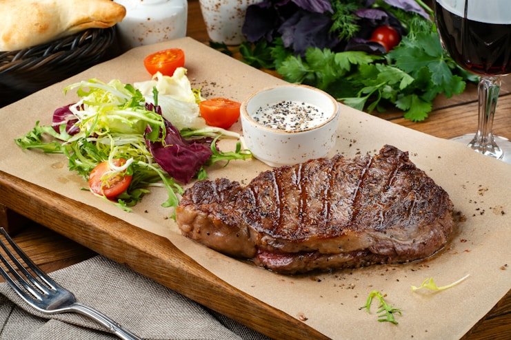 A juicy steak served with fresh salad and rustic bread on a wooden board.
