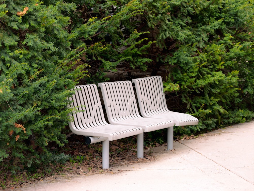 a row of white park benches next to a bush