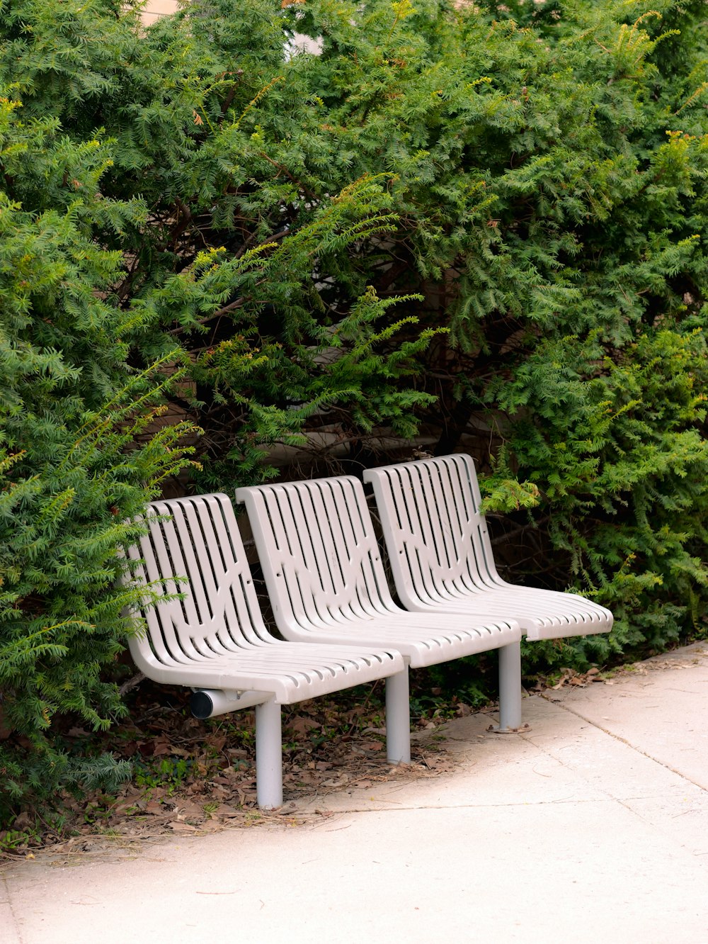 a couple of white benches sitting next to a bush