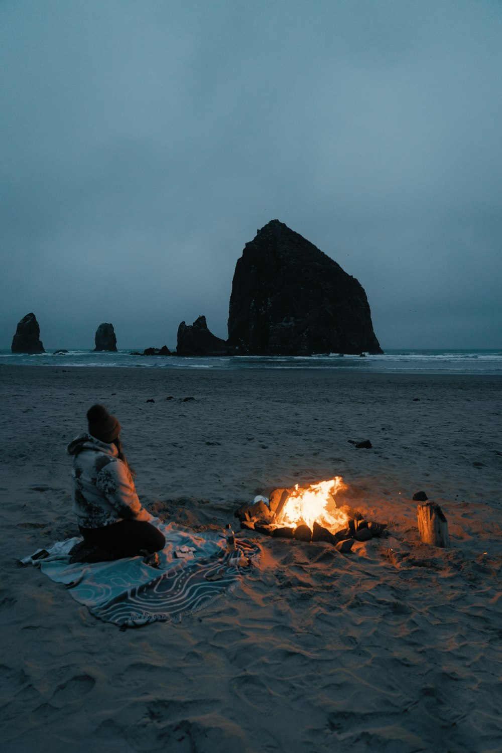 a person sitting next to a campfire on a beach