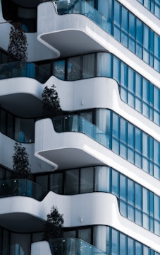 A modern building facade with a series of curved balconies, glass panels, and a sleek architectural design. Trees are placed on the balconies, adding a touch of greenery to the urban structure.