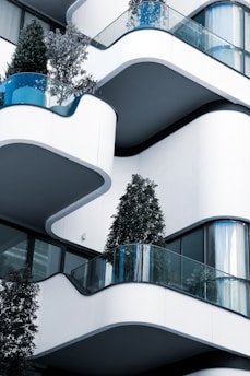 A modern building with curved balconies features glass railings and trees on each level, contributing to a green architectural design.