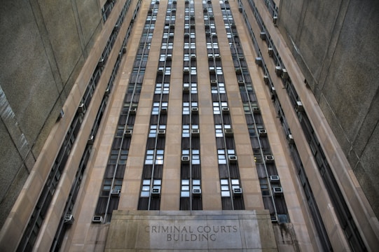 A towering building with numerous windows and air conditioning units. The structure is made of concrete and appears to be part of an urban setting. The words 'Criminal Courts Building' are visible at the base of the building.