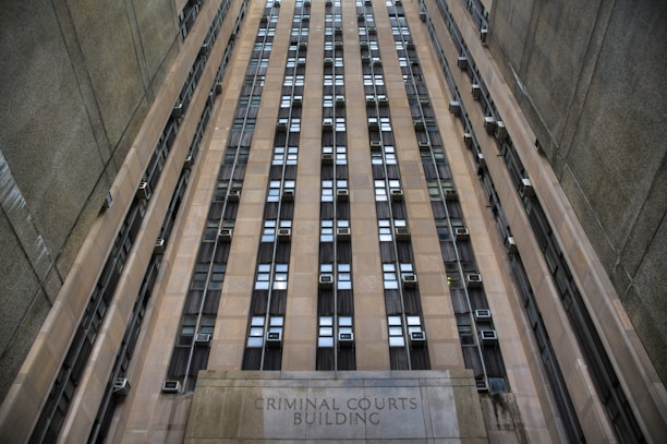 A towering building with numerous windows and air conditioning units. The structure is made of concrete and appears to be part of an urban setting. The words 'Criminal Courts Building' are visible at the base of the building.
