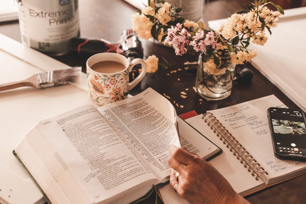 una persona seduta a un tavolo con un libro e una tazza di caffè