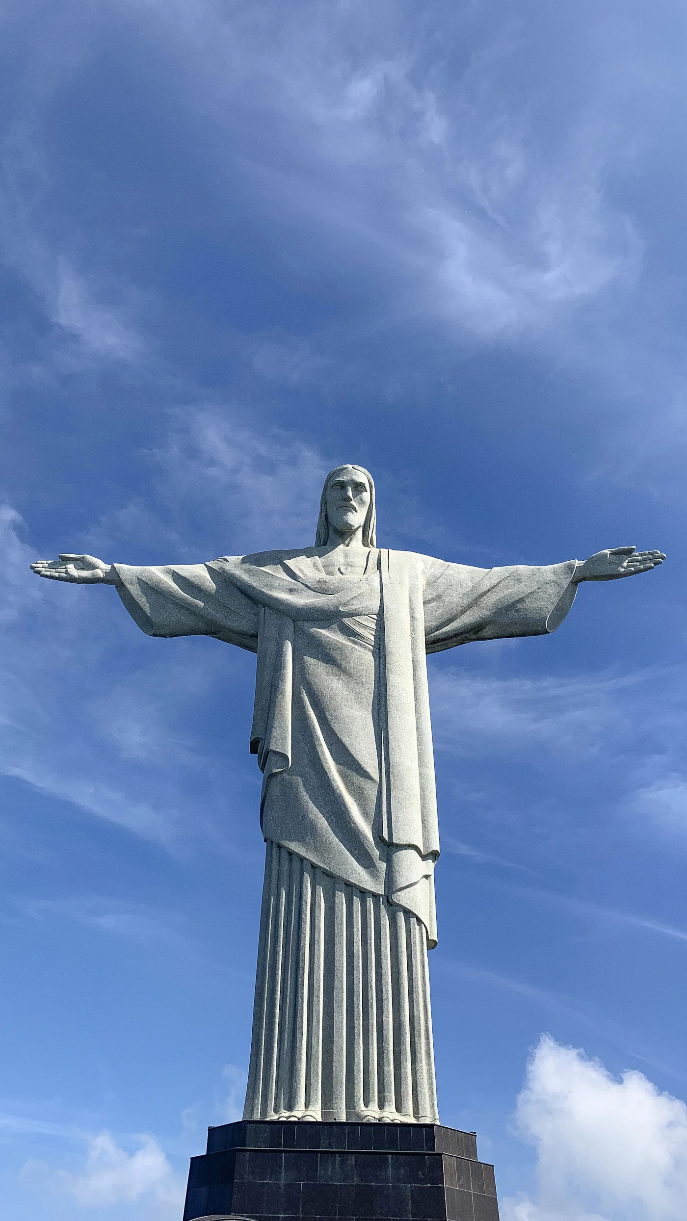 Christ the Redeemer statue on Corcovado mountain in Rio de Janeiro with arms outstretched against a dramatic sky with the city and Guanabara Bay and Sugarloaf mountain visible below in the hazy distance