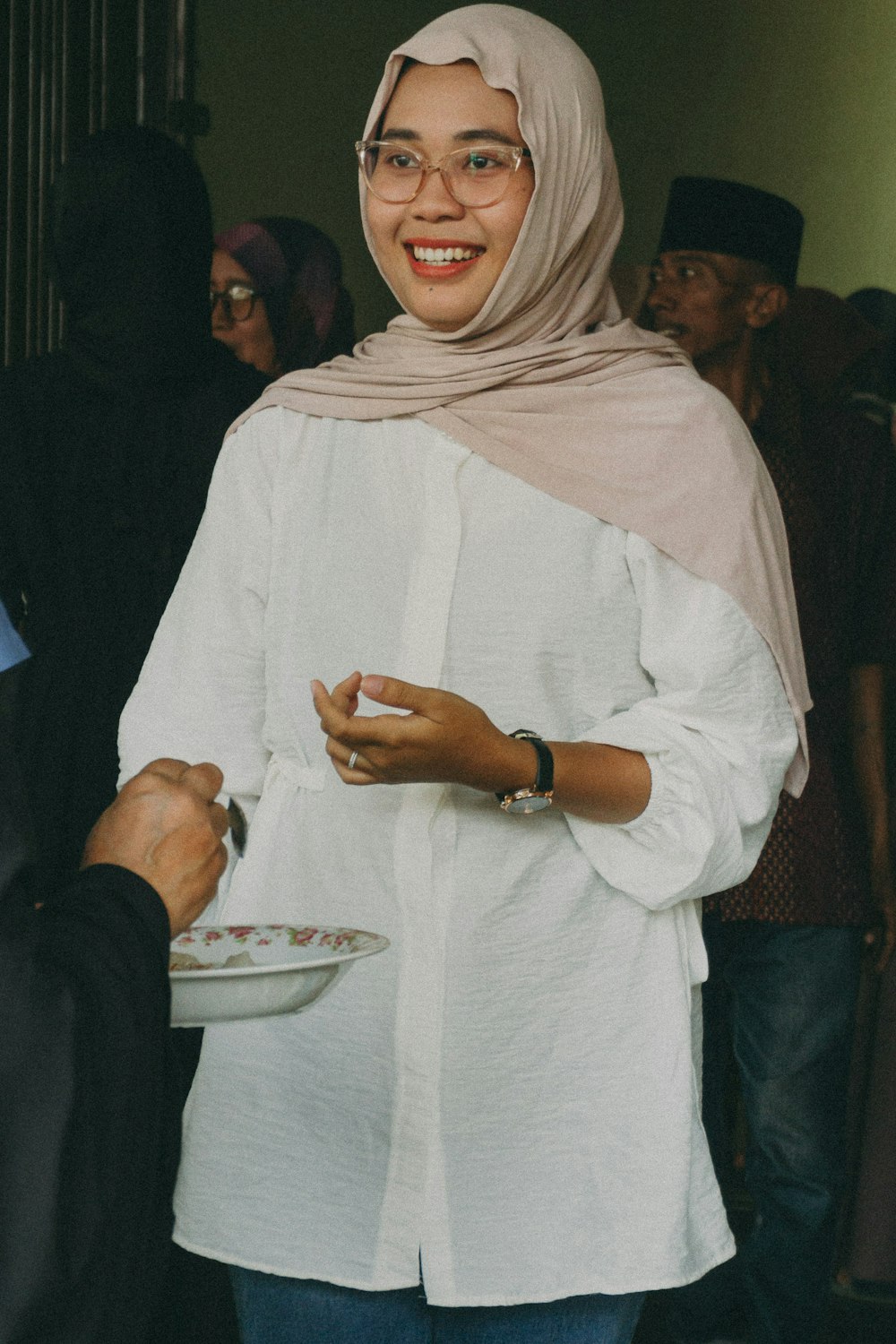 a woman in a hijab smiles as she holds a plate of food
