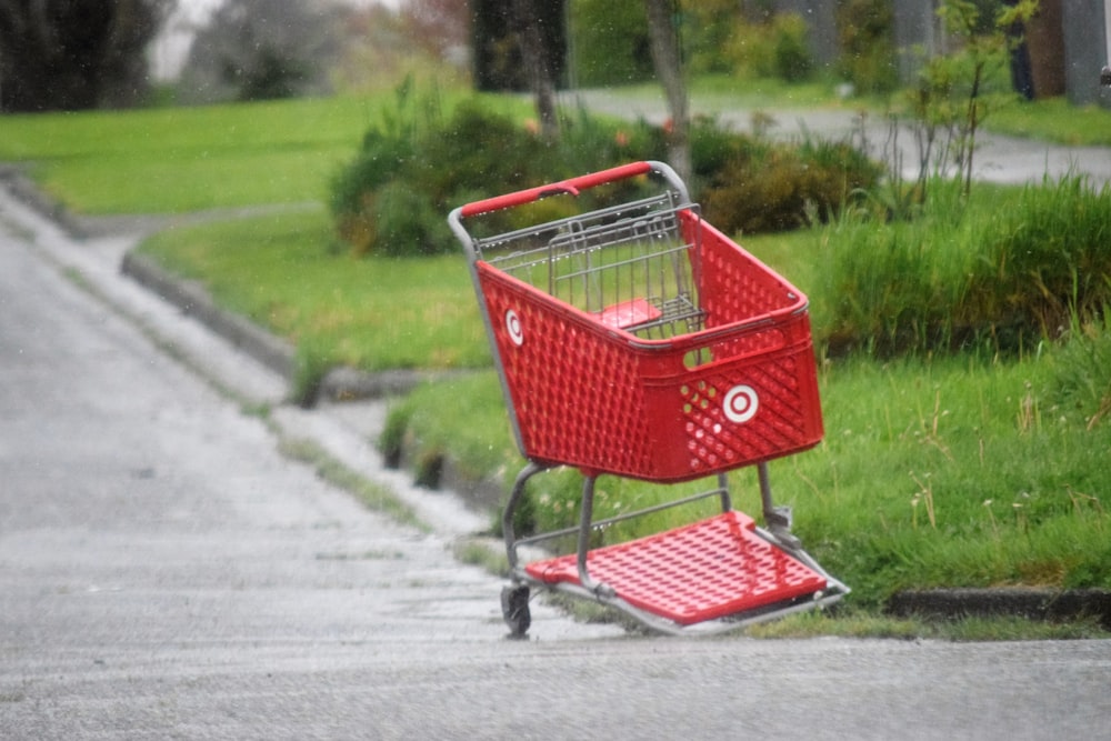 a red shopping cart sitting on the side of a road