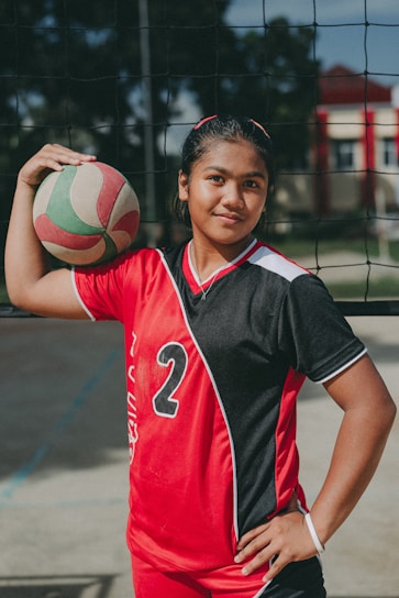 A cheerful portrait of Ayesha in her volleyball uniform holding her black belt proudly.
