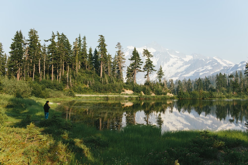 a person standing in front of a lake surrounded by trees