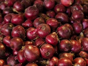 A large pile of fresh red onions with visible roots, showcasing a vibrant color palette of deep reds and purples.