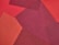 A collage of fabric pieces in varying shades of red, arranged in overlapping geometric patterns. Textures of the fabrics are visible, contributing to a layered and tactile appearance.