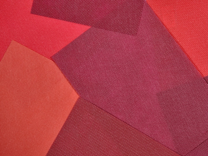 A collage of fabric pieces in varying shades of red, arranged in overlapping geometric patterns. Textures of the fabrics are visible, contributing to a layered and tactile appearance.