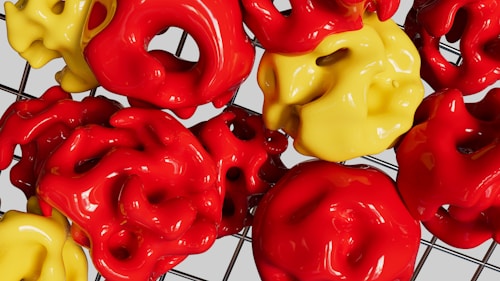 A collection of glossy, abstract shapes predominantly in red and yellow colors, arranged on a grid-like background. The shapes have irregular, curvy surfaces creating a vibrant and dynamic visual effect.