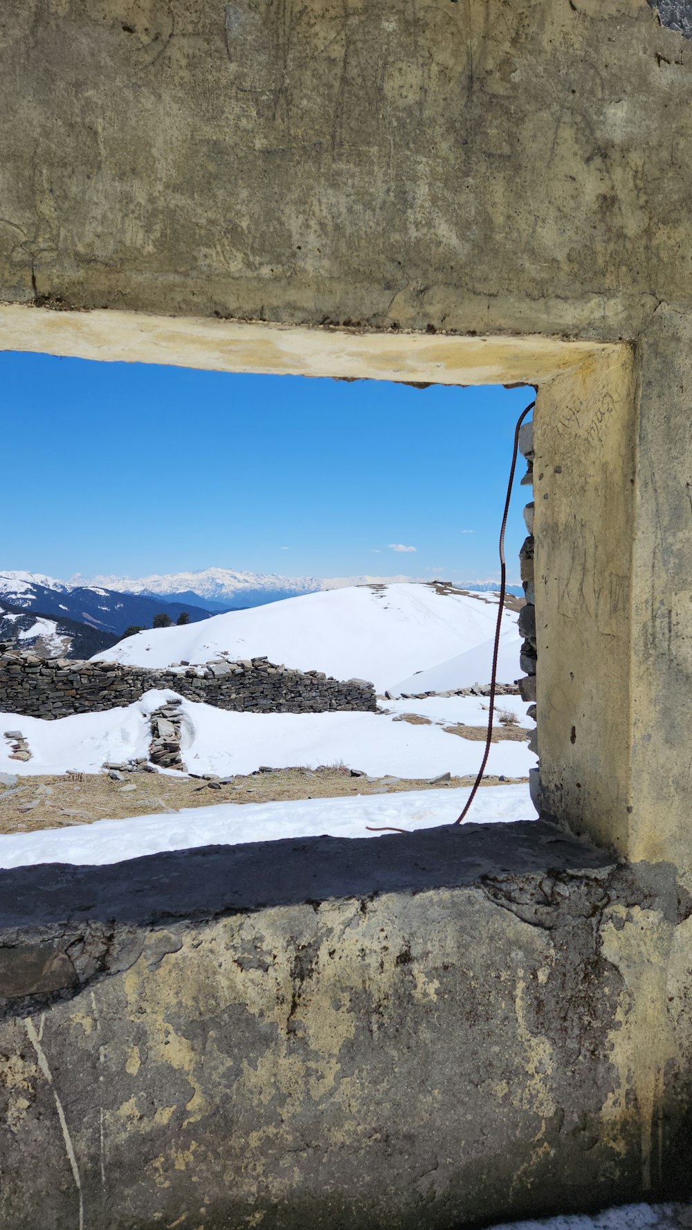 a window in a stone wall with a view of a snowy mountain