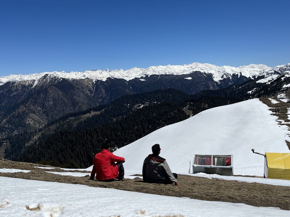 a couple of people sitting on top of a snow covered slope