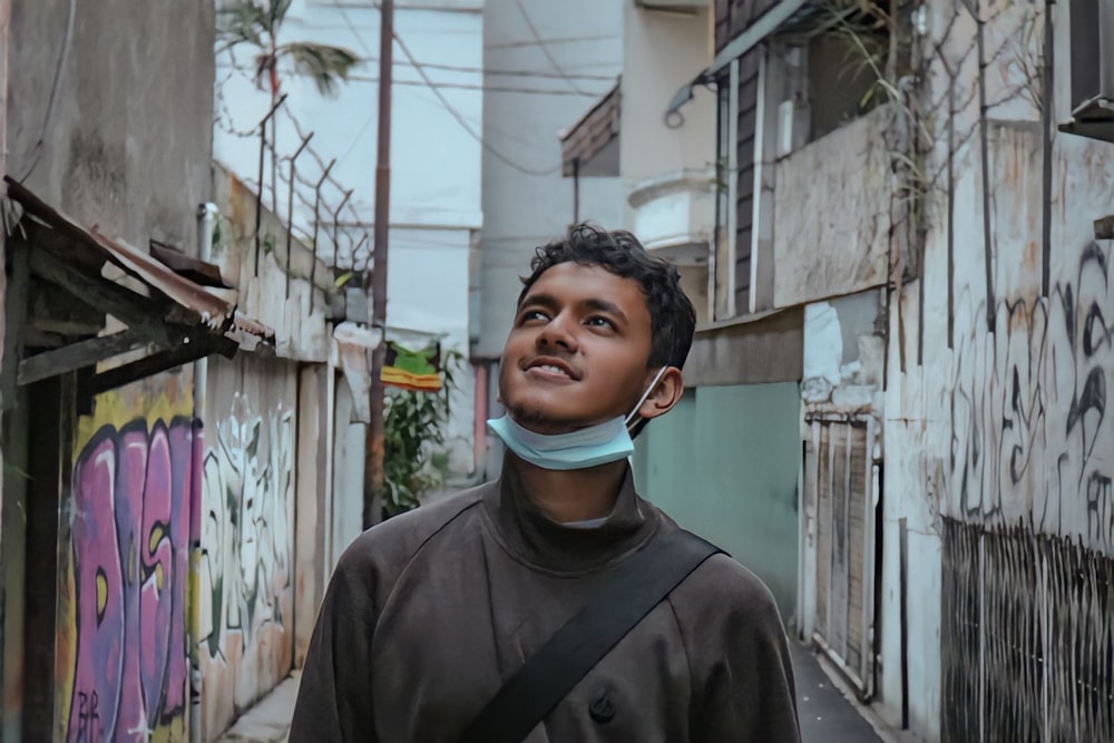 a young man wearing a neck gaiter in an alleyway