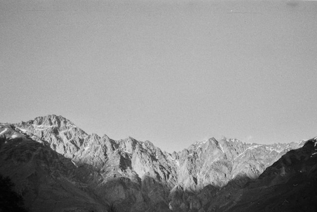 A grayscale image of a rugged mountain range with jagged peaks under a clear sky.