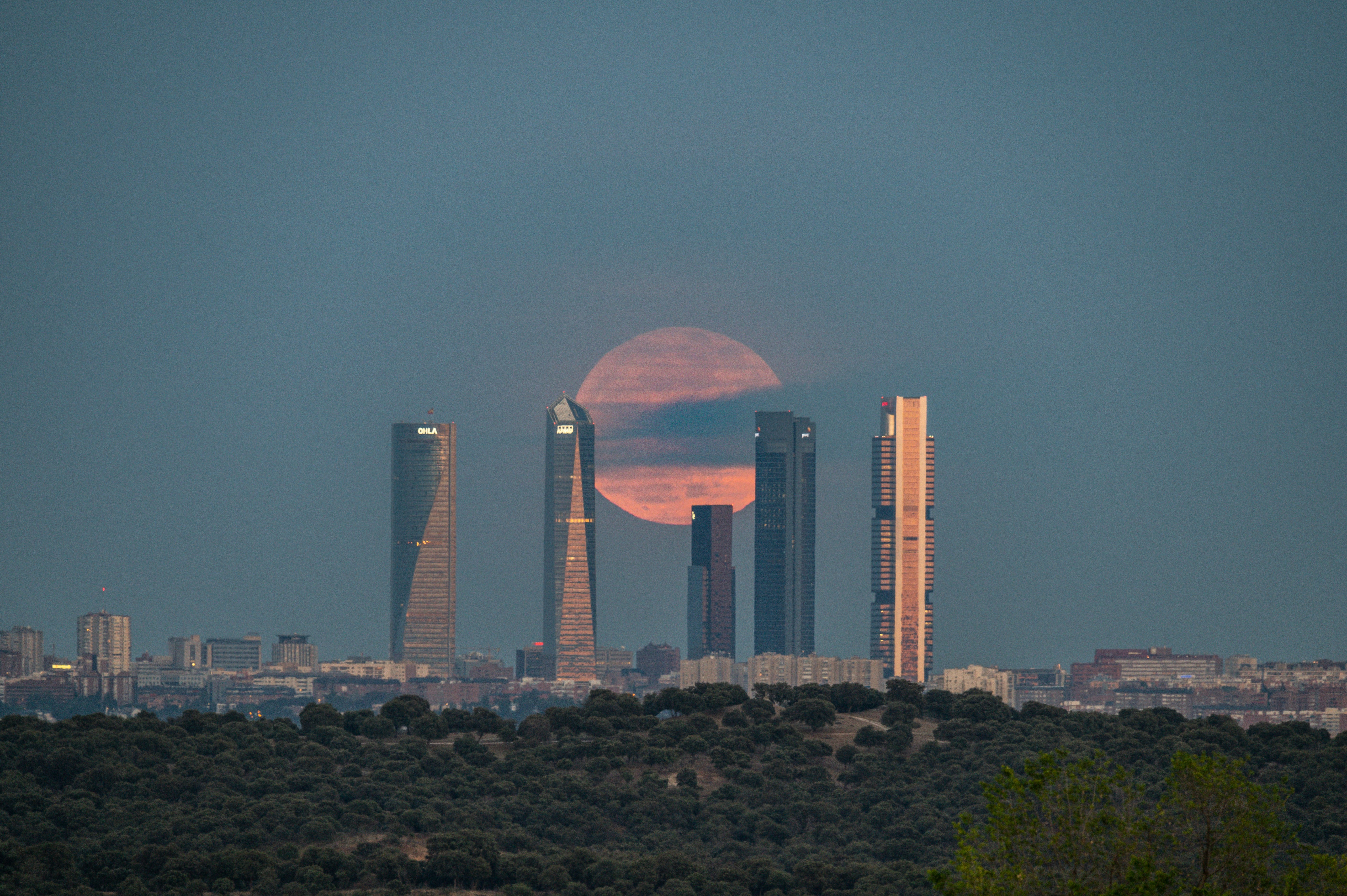 a full moon rising over a city with tall buildings, 