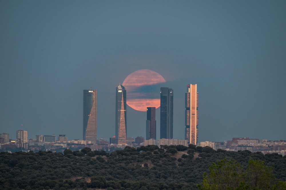 Una luna llena que se eleva sobre una ciudad con edificios altos