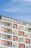 The image features a modern multi-story building with a prominent sign displaying 'Binghatti' at the top. The structure has a repetitive design with square balconies, each having glass railings and a distinctive orange back wall. The building stands against a clear blue sky.