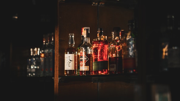 Rustic wooden shelf displaying a variety of artisanal liquor bottles with warm amber lighting