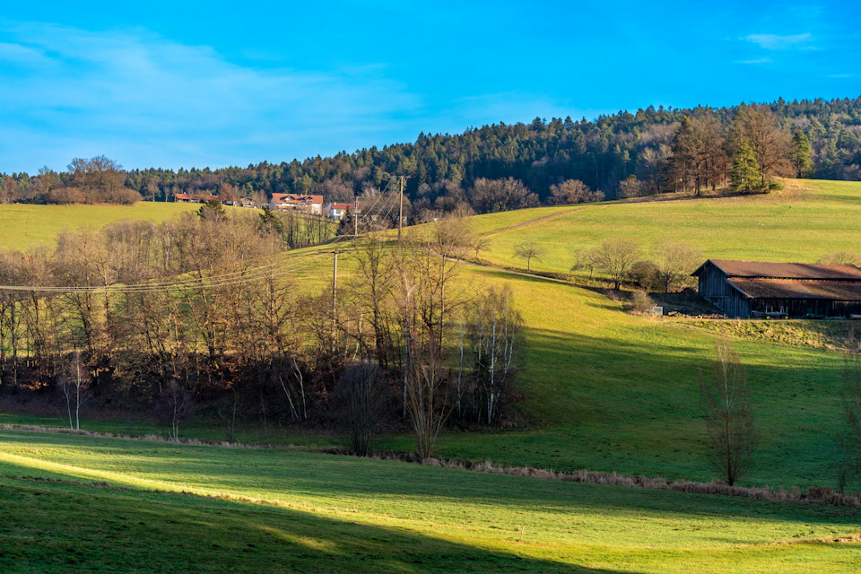 Serene countryside landscape features rolling hills, lush green grass, and a small village in distance