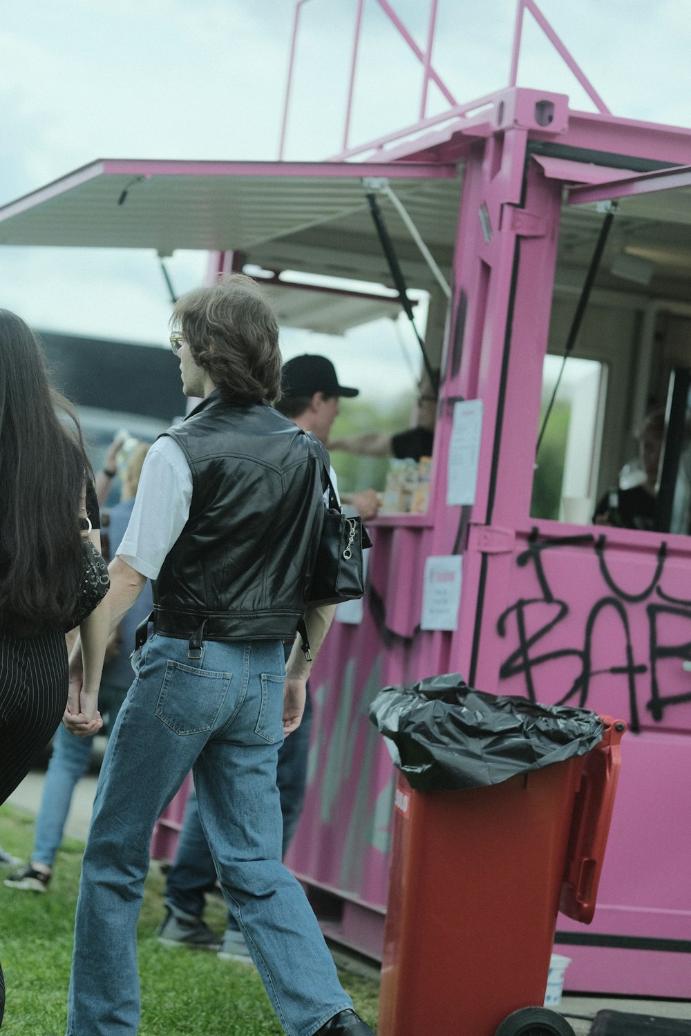 a group of people standing around a pink food truck